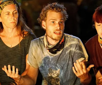 "Three people at a tense discussion on Australian Survivor, one with a cat print shirt gesturing animatedly."