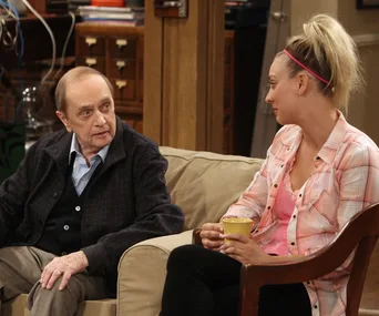 Two characters sit on a couch, engaged in conversation. One holds a mug. Scene from "The Big Bang Theory," Season 12.