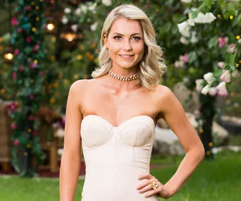 A woman in a strapless dress stands outdoors, smiling, surrounded by flowers and decorative lights.