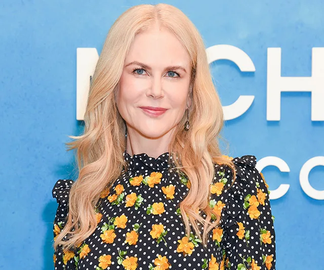 Woman with long blonde hair in a floral dress poses in front of a blue background at a movie event.