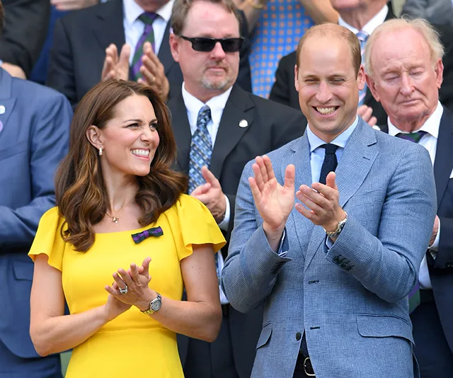 A woman in a yellow dress and a man in a blue suit clapping at an event, surrounded by other applauding people.
