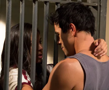 A woman and a man embrace through jail bars, conveying emotion.