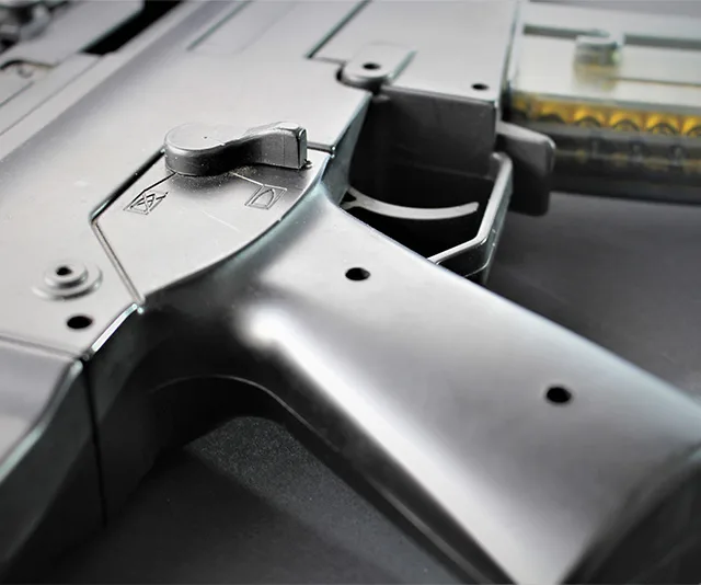 Close-up of a black firearm's trigger and safety selector on a flat surface.