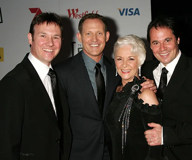 Four people in formal attire smiling at an event with sponsor logos in the background.