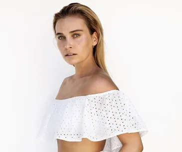 Person in a white off-shoulder top against a plain background, facing the camera with a neutral expression.