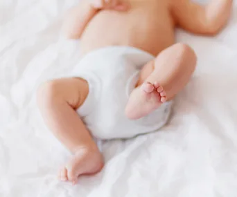 A baby in a diaper lying on its back on a white sheet.