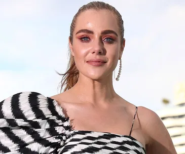 A person in a black and white patterned outfit with pearl earrings, standing outdoors on a sunny day.