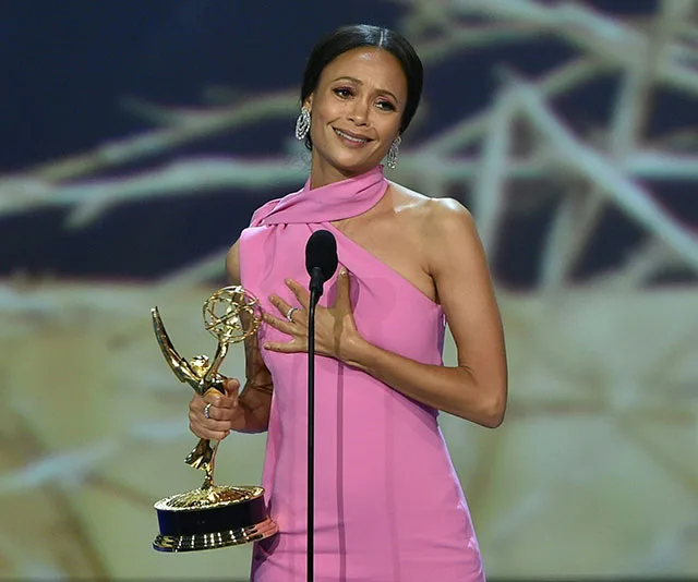 Woman in pink dress holding Emmy award on stage, giving acceptance speech.