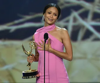 Woman in pink dress holding Emmy award on stage, giving acceptance speech.