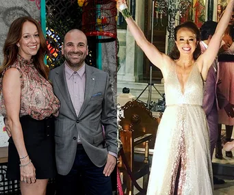 Couple posing at an event; woman in elegant dress celebrating with arms raised inside a venue.