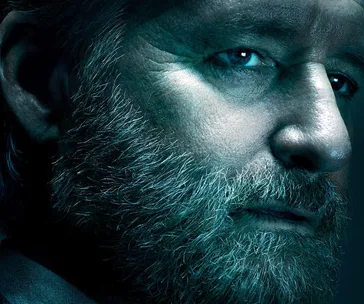 Close-up of a serious, bearded man in moody lighting, possibly a character from "The Sinner" Season 2.