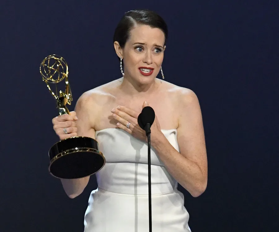 Claire Foy giving an acceptance speech at the Emmys, holding the award, wearing a white dress.