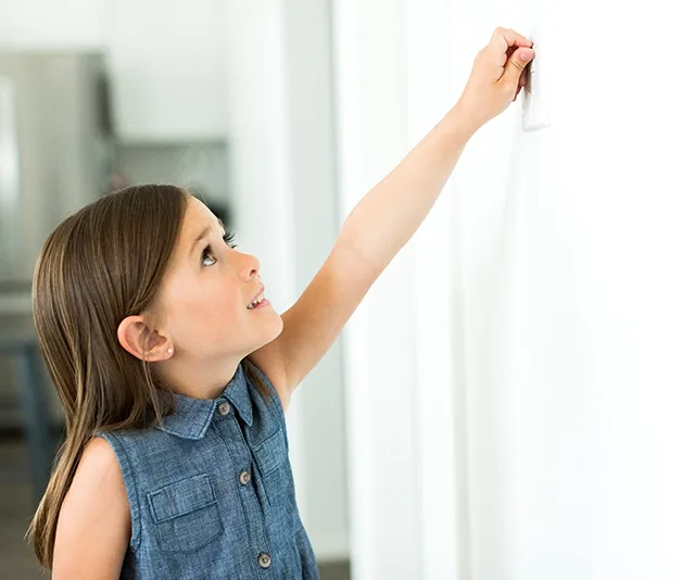 Girl reaching up to turn off a light switch in a bright room.