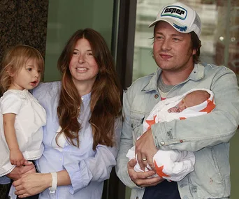 Family with two young children, one child held by a woman, and a baby wrapped in a star-patterned blanket held by a man.