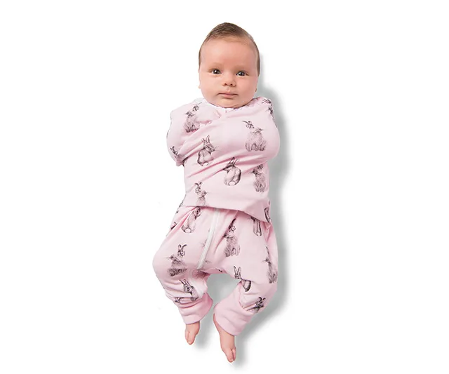 A baby swaddled in pink fabric with bunny prints, lying with arms wrapped snugly.