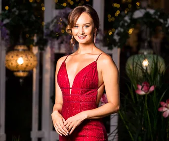 Woman in a red dress smiling at a formal event with floral and light decorations in the background.