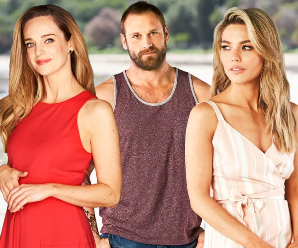 Three characters from "Home and Away" stand together, two women in dresses and a man in a tank top look contemplative.