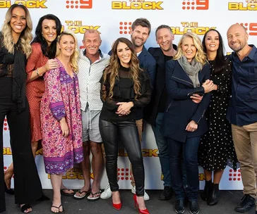 A group of twelve people smiling at a promotional event for "The Block," standing in front of a branded backdrop.