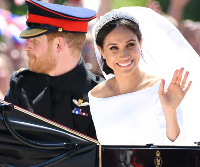 Royal couple in carriage; bride in white dress waves, groom in military uniform with red cap looks sideways.