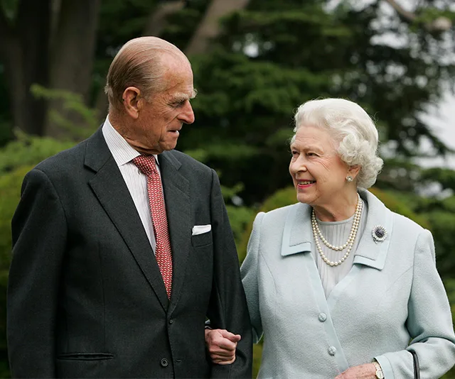 Elderly man and woman walking arm in arm, smiling at each other in a garden setting.