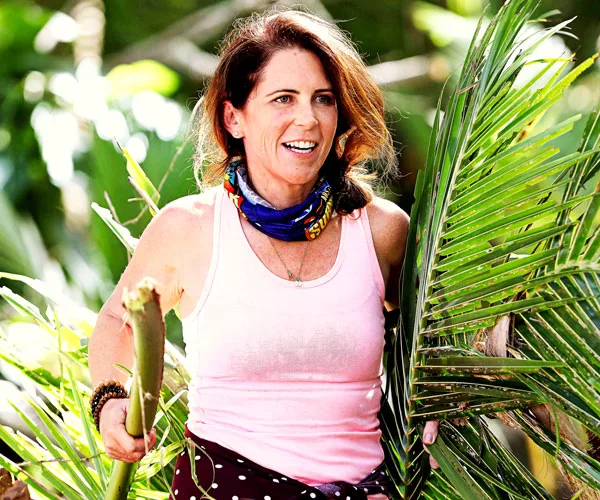 Woman in a pink tank top holding palm leaves, outdoors with a determined expression, from Australian Survivor.
