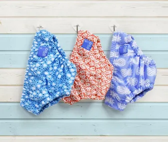 Three colorful reusable swim diapers with different patterns hanging on hooks.