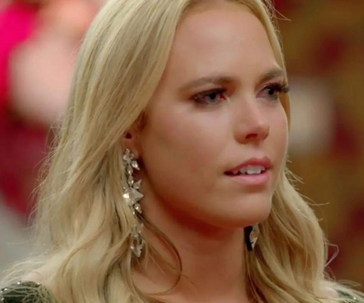 A woman with long blonde hair and tearful eyes, wearing large, dangling earrings.