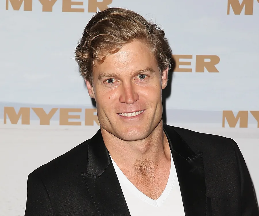 Man in a black blazer and white shirt smiling at an event with "MYER" in the background.