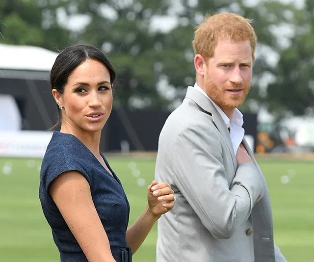 A woman in a blue dress and a man in a gray suit walk outdoors, glancing back at the camera.