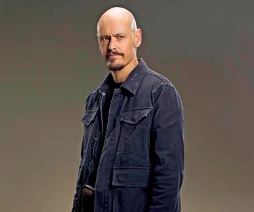 Man in a dark jacket, posing with a determined expression against a neutral background.