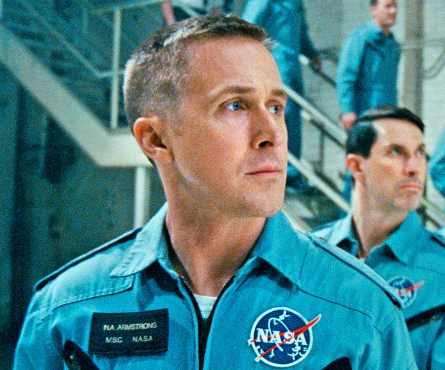 Ryan Gosling as Neil Armstrong in a blue NASA uniform from "First Man," looking to the side.