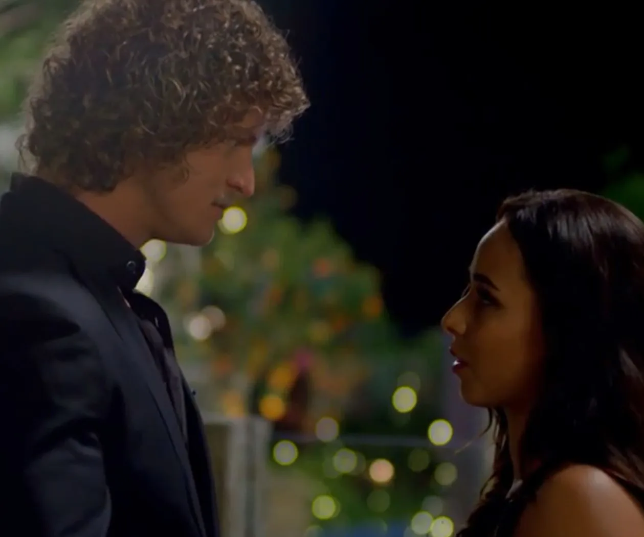 Man and woman facing each other at night with blurred lights in the background.