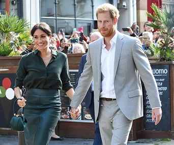 Couple walking hand-in-hand, surrounded by onlookers with cameras, in an outdoor setting.
