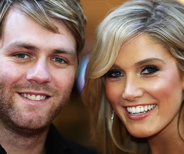 Two people smiling closely, one with light brown hair and a beard, and the other with blonde hair and wearing earrings.