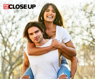 Two people outdoors, one giving a piggyback ride, both smiling against a blurry tree background.