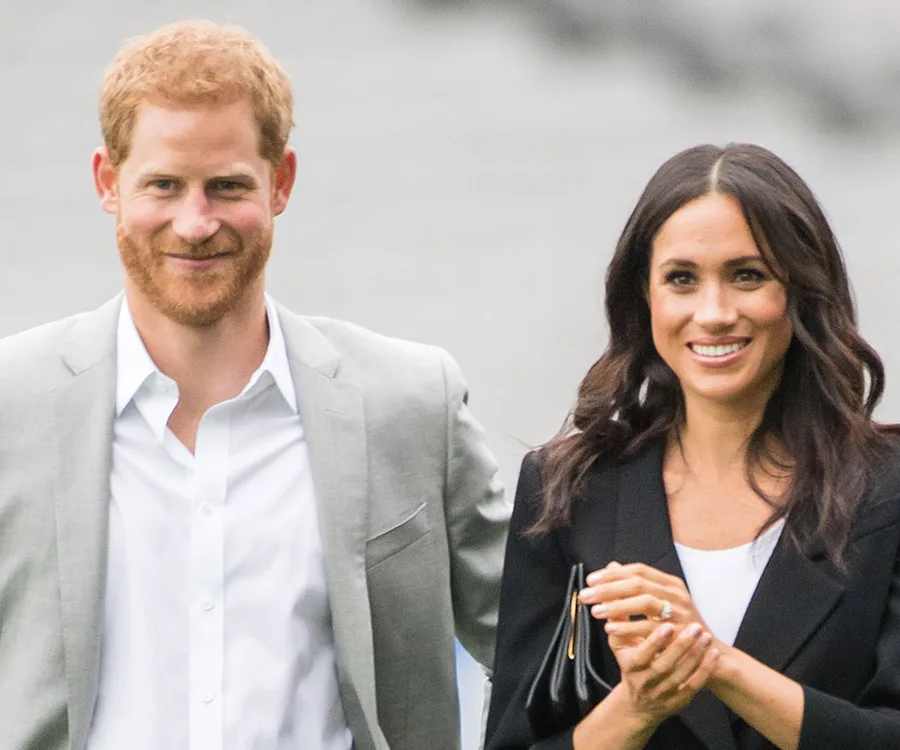 Image of a smiling couple, one wearing a light gray suit and the other in a black blazer, walking together outside.