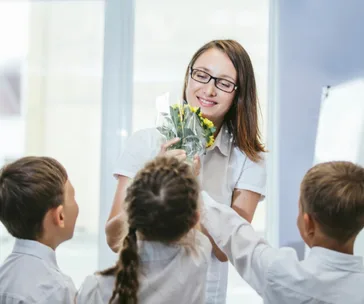 Teacher receiving flowers from smiling students in a classroom.