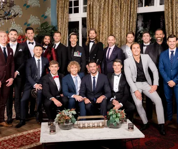 A group photo of 18 men in formal attire from "Bachelorette Australia 2018" set, posing inside a decorated room.
