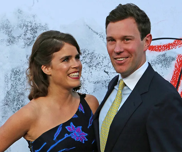 A woman in a floral dress smiling at a man in a suit with a patterned tie, posing in front of an abstract backdrop.