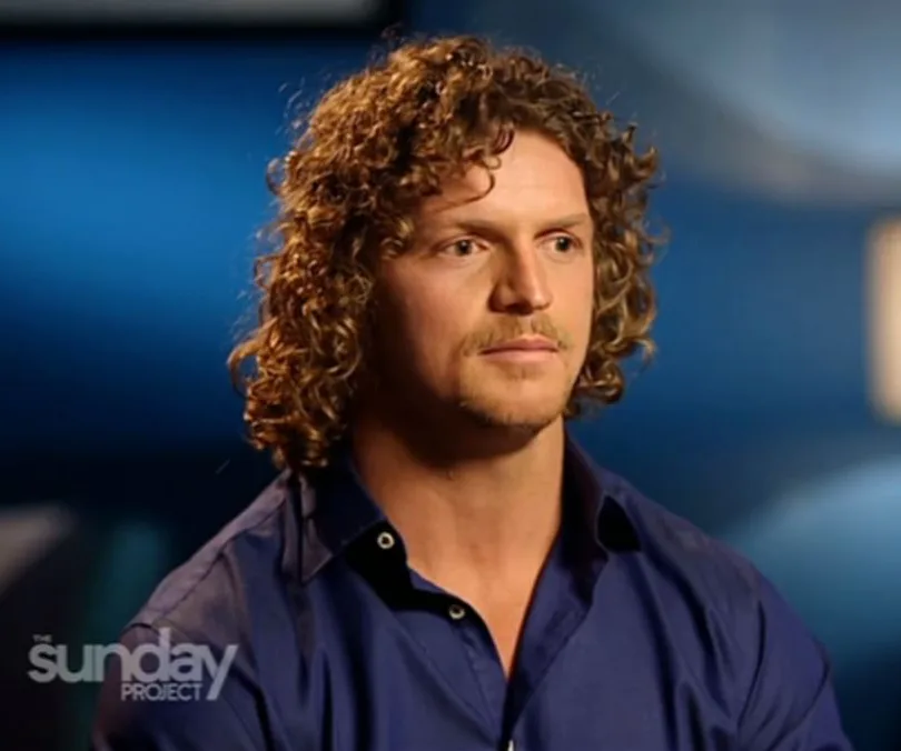 Man with curly hair and mustache in a blue shirt sits against a blue background. "The Sunday Project" logo in corner.