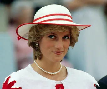 A woman in a red-trimmed white hat and pearl necklace smiles, wearing a red and white outfit.