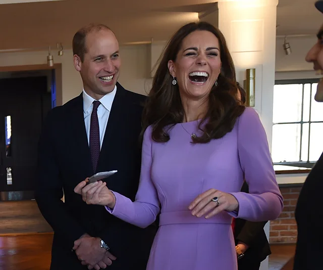 A man and a woman, both in formal attire, smiling and laughing at a public event indoors.