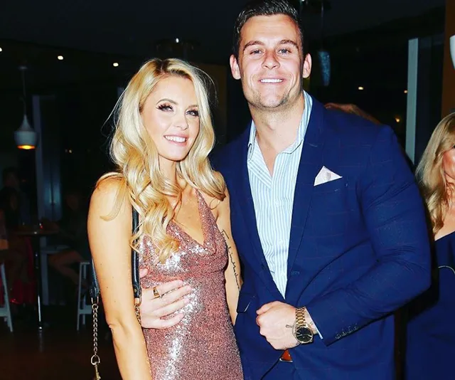 Couple posing together, with the woman in a sparkly dress and the man in a blue suit, smiling at the camera.