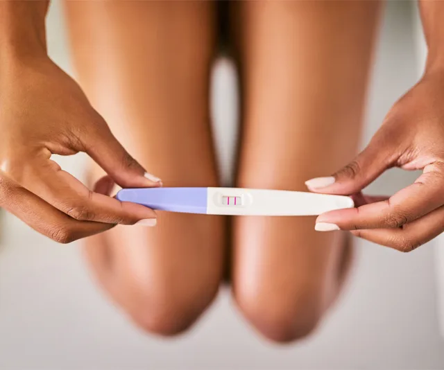 "Close-up of hands holding a positive pregnancy test with two pink lines."