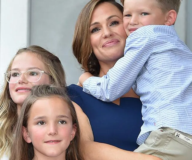 A woman smiling with three children, two girls and a boy, posing happily together.