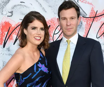 A couple posing together at an event; woman in a patterned dress, man in a suit with a yellow tie.