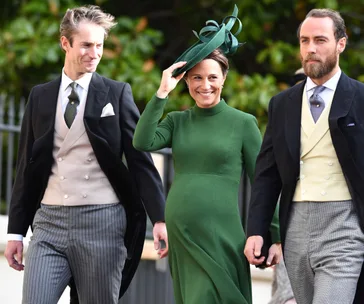 Three people in formal attire attending a wedding; a woman in a green dress and hat is smiling.