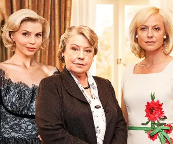 Three women from "A Place to Call Home" series standing together in elegant attire, in a warmly lit room.
