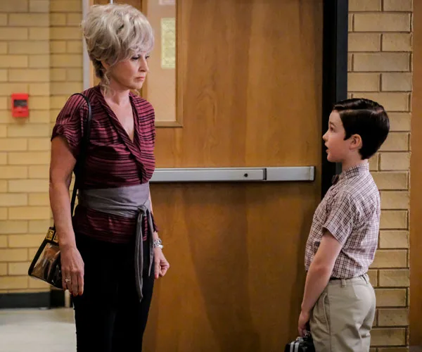 Grandmother and young boy talking in a school hallway, standing near a wooden door.