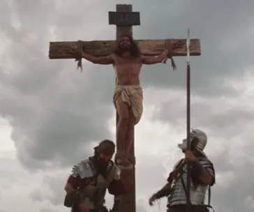 Man on a cross labeled "INRI," with two Roman soldiers standing by, under a cloudy sky.